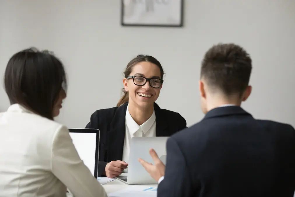 Smiling team members meeting around a table with laptops